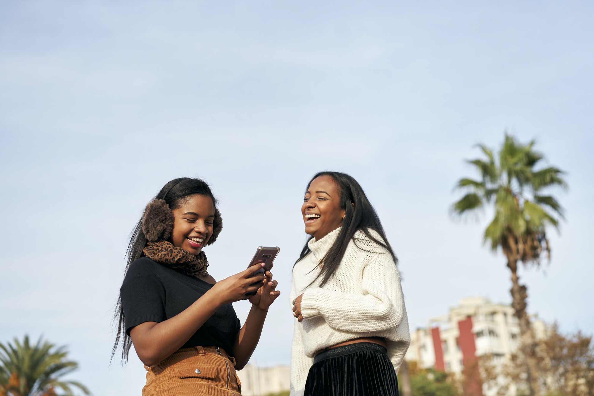 Two black girls using a mobile phone and laughing. People and technology concept with smartphone.